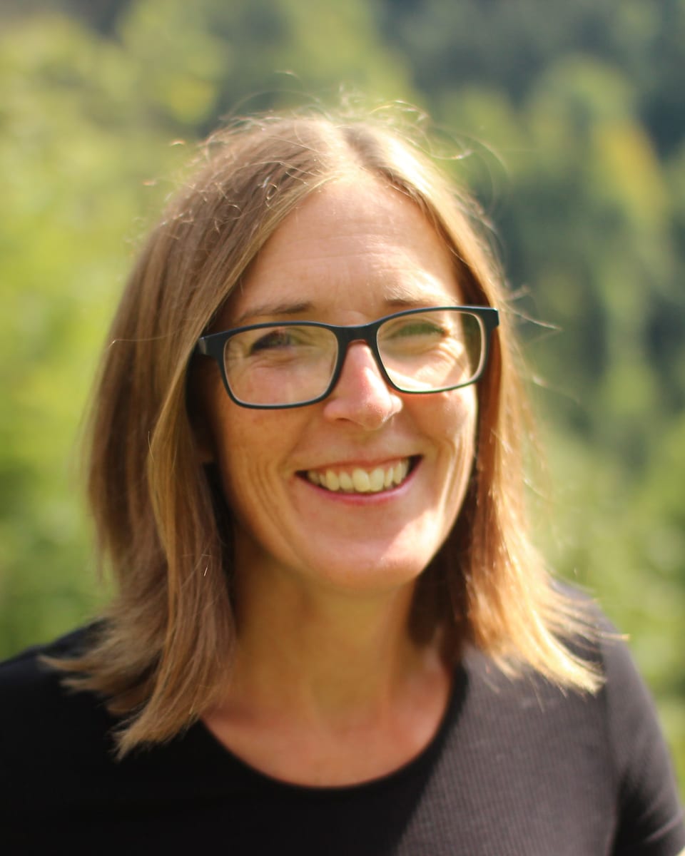 Belinda Bateson, life coach, smiling outdoors in front of green foliage